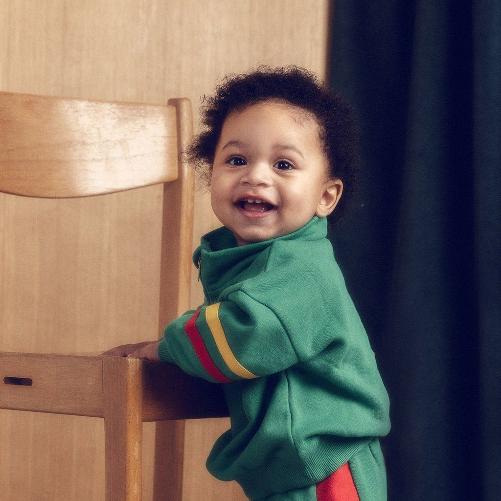 Mini Rodini E. T. limited release green sweatshirt | half-zip front | standup collar | red & yellow stripes on sleeves | banded at wrist & waist | modeled on Toddler