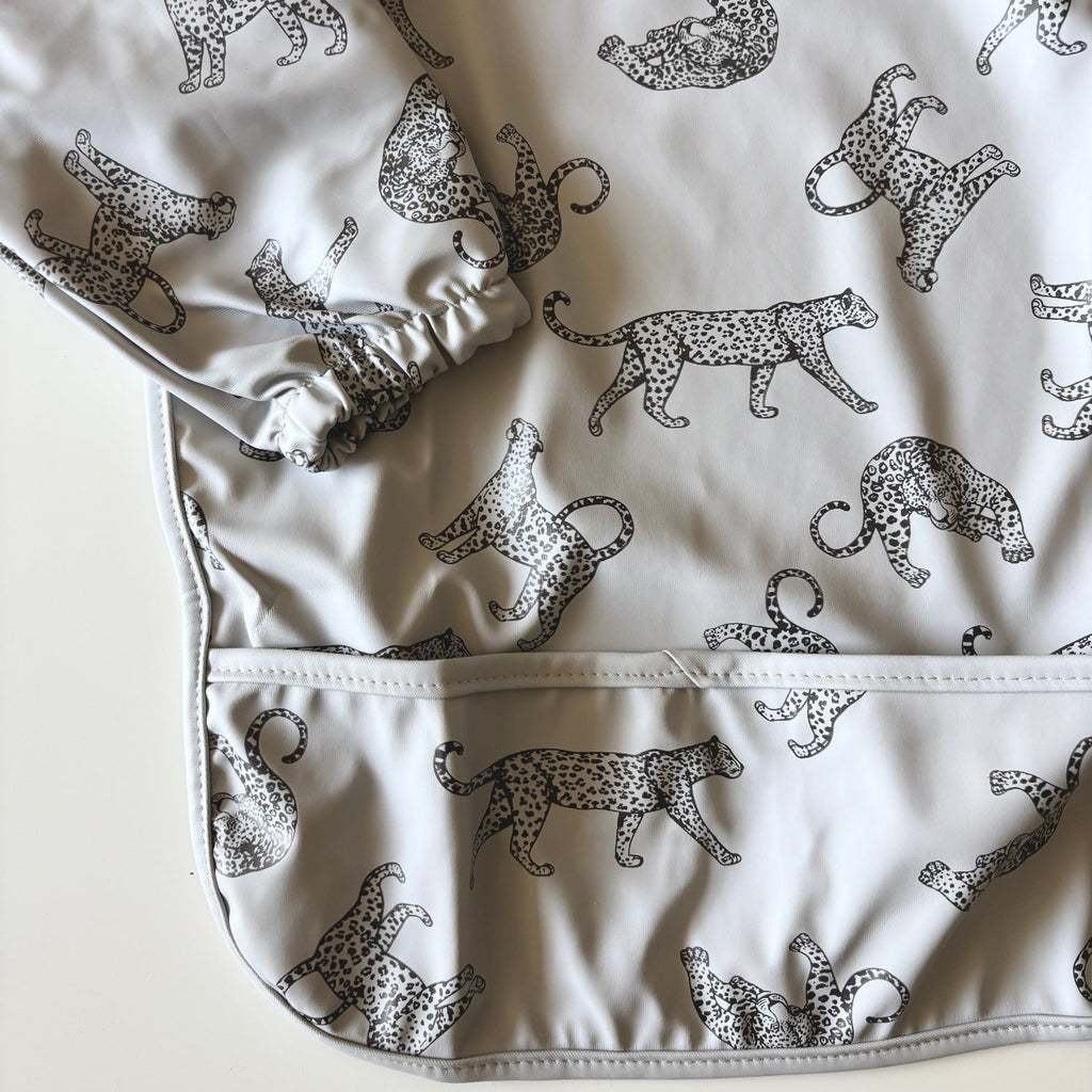 Baby bib with black cheetah print on a light gray background | long sleeves | snaps at back of neck | pocket for catching crumbs | closeup