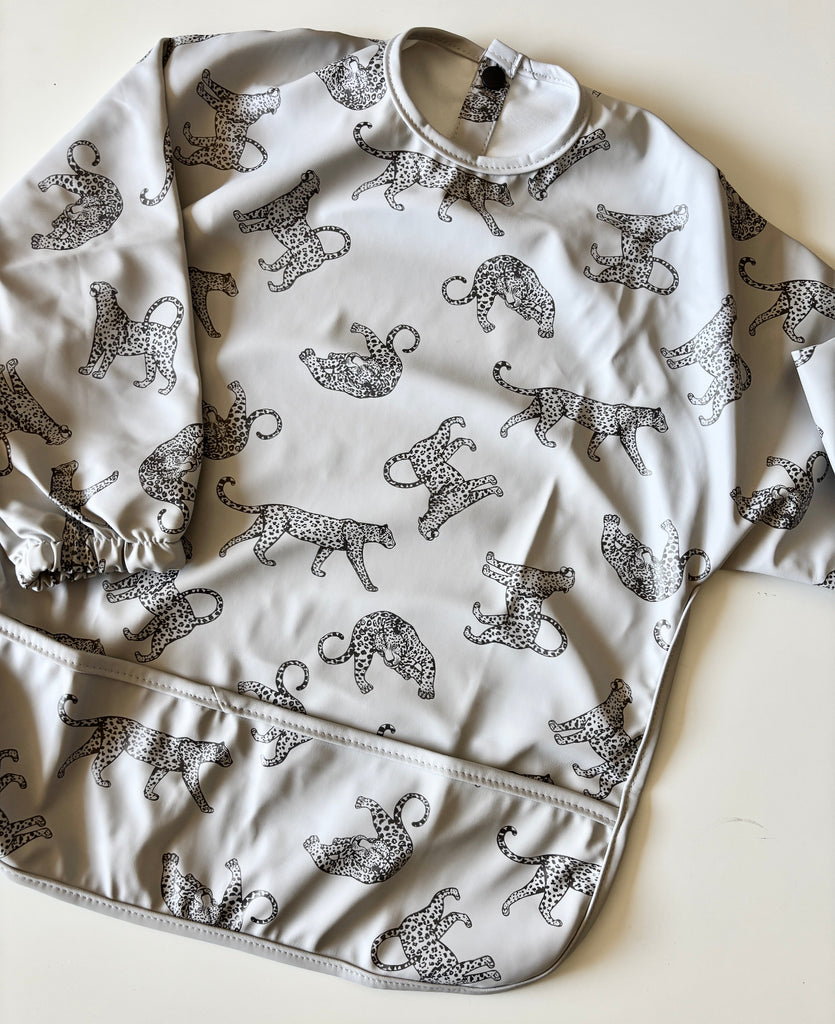 Baby bib with black cheetah print on a light gray background | long sleeves | snaps at back of neck | pocket for catching crumbs