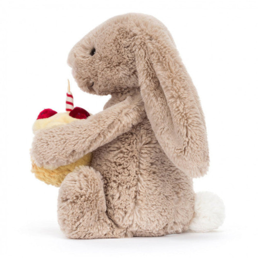 Bashful Bunny holding a tiny, textured amuseables birthday cake, topped with soft cream icing, velveteen strawberries, and a striped candle | 12" long | sits 9" high | Long ears | side view