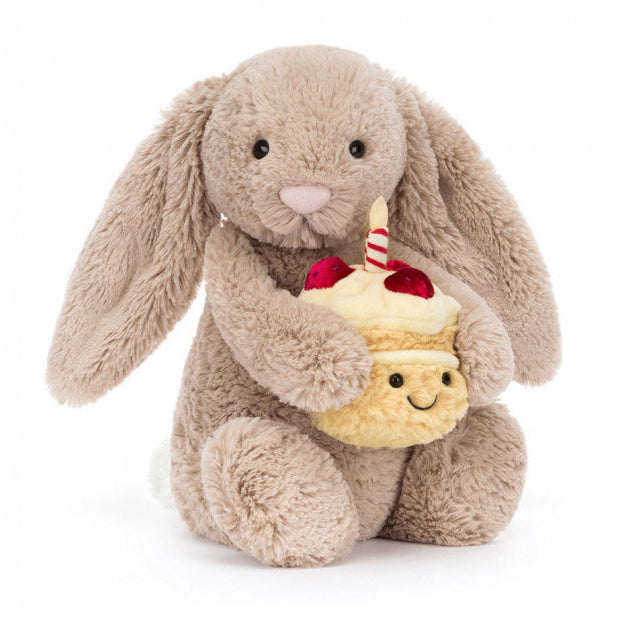 Bashful Bunny holding a tiny, textured amuseables birthday cake, topped with soft cream icing, velveteen strawberries, and a striped candle | 12" long | sits 9" high | Long ears | Hard eyes