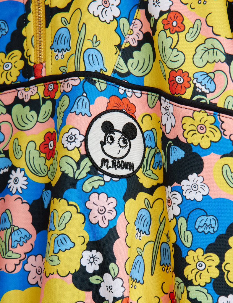 Colorful floral-patterned track pant in soft polyester. Half-zip front, black piping in front, stand-up collar, no-seam sleeve, ribbed at wrist and waist. Top quality Mini Rodini brand |closeup